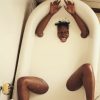 Person submerged in milky bathwater with head, arms, and legs above the surface, grinning playfully and sticking out tongue.
